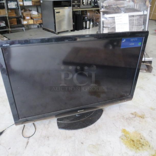 Sharp Aquos flat-screen TV, black, on stand, showing "INPUT5 HDMI" on screen, used condition, power cable visible.