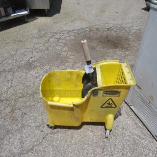 Yellow Rubbermaid mop bucket with wringer on wheels, used condition. Features caution sign and label with model info.
