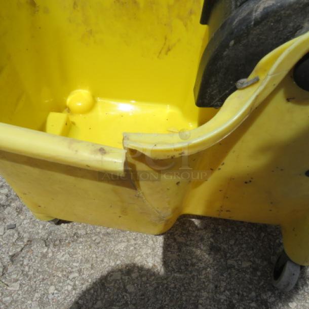 Yellow mop bucket with visible dirt and damage on the rim, some scuff marks and scratches; on caster wheels.