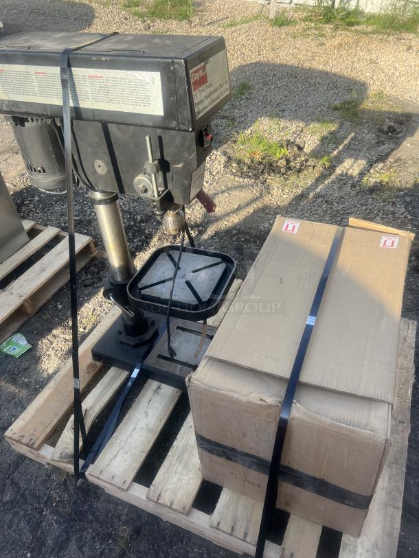 Dayton 15" Drill Press, model visible, mounted on a pallet beside a strapped cardboard box, shown outdoors.