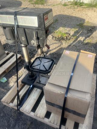Dayton 15" Drill Press, model visible, mounted on a pallet beside a strapped cardboard box, shown outdoors.