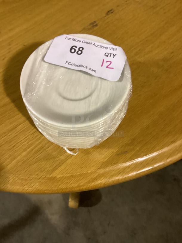 Set of 12 white 5-1/2" dessert saucers, wrapped, with auction tag "68 QTY 12" on top, indicating auction details.