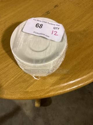 Set of 12 white 5-1/2" dessert saucers, wrapped, with auction tag "68 QTY 12" on top, indicating auction details.