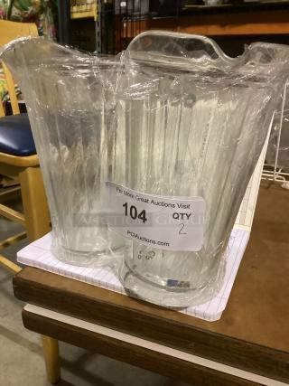 Two clear plastic juice pitchers, 9-inch height, wrapped in plastic, label indicates quantity 2, item number 104.
