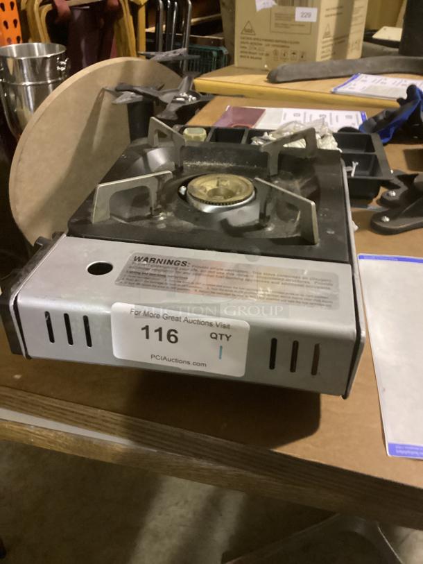 Portable butane stove, 13-5/8”, with metal housing and grate. Visible warning labels and auction sticker "116 QTY 1".