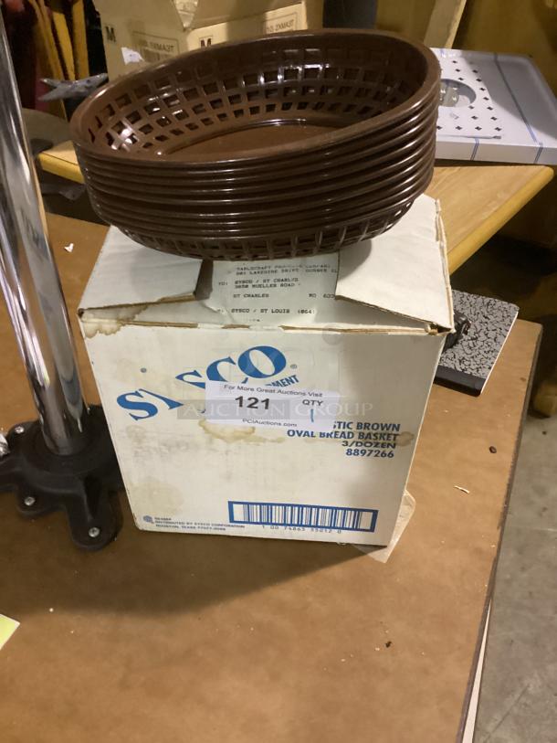 Plastic brown oval bread basket, good condition, stacked on a Sysco box labeled "Plastic Brown Oval Bread Basket 3/Dozen."