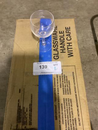 Small wine glass, 5-3/8 inches, clear, resting on cardboard labeled "Glassware Handle With Care," auction tag visible.