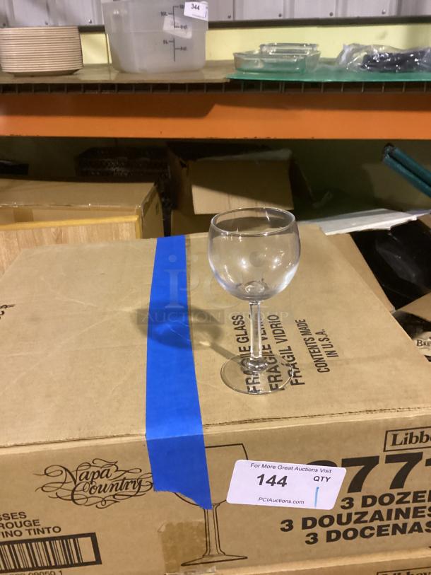 Red wine glass, 8-1/2 inches, clear glass, placed on a Napa Country branded box marked "fragile." Auction label "144" visible.