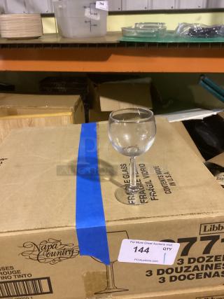 Red wine glass, 8-1/2 inches, clear glass, placed on a Napa Country branded box marked "fragile." Auction label "144" visible.