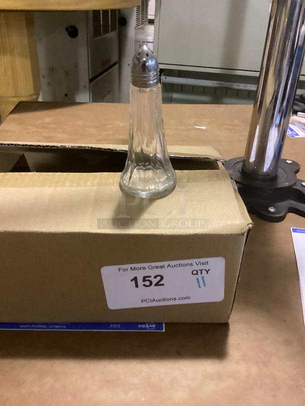 Small glass salt shaker with metal lid, 4-1/2" tall, on a cardboard box marked "152 QTY 11" from PCI Auctions.