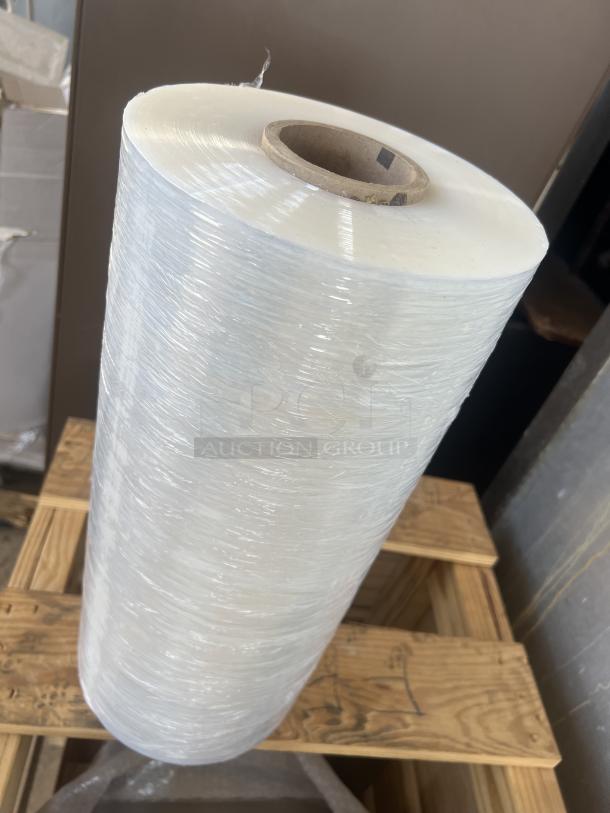 Roll of shrink wrap on a wooden pallet, tightly wound, clear plastic, with a cardboard core, indicating new condition.