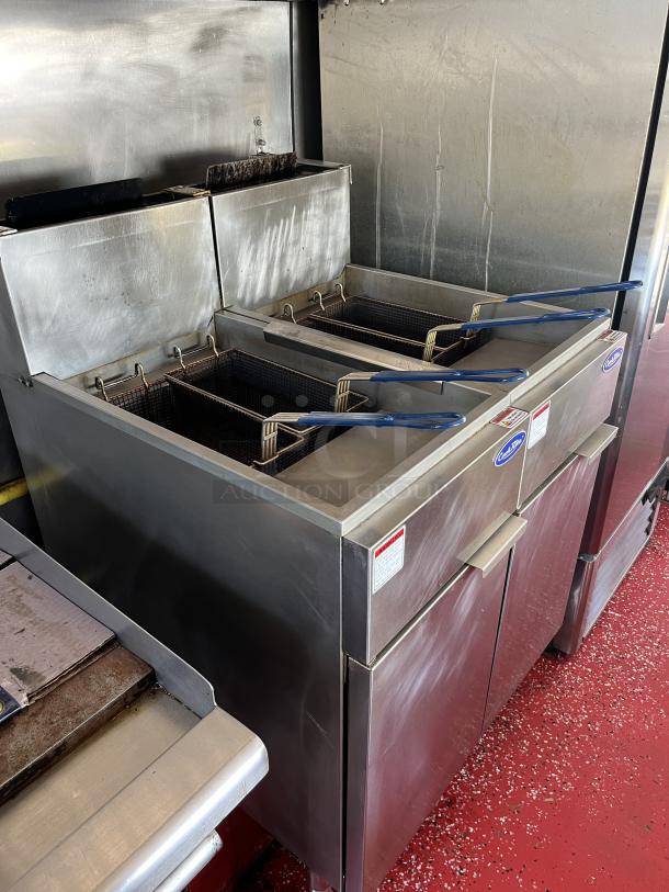 Commercial double deep fryer with stainless steel finish, blue handles, and visible safety and brand labels. Good condition.