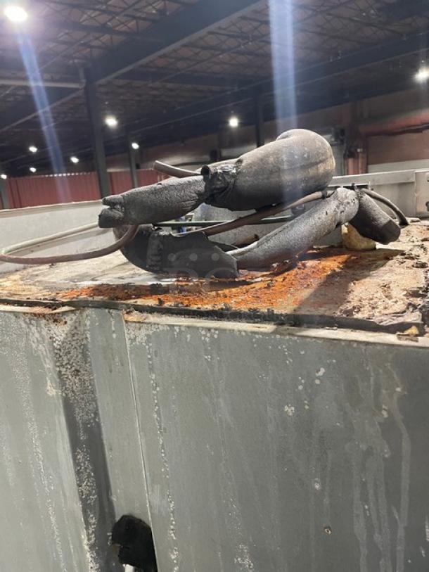 Industrial equipment with visible wear and rust, possibly a worn hose assembly on a corroded metal surface in a factory setting.