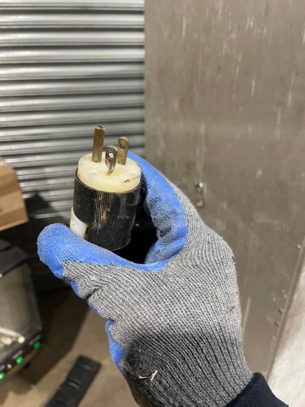 Industrial plug in work glove, worn condition, three-prong, black and white housing, visible wear and dirt marks.