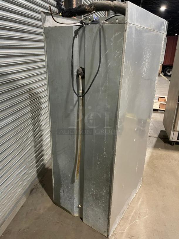 Commercial metal refrigeration unit, industrial-style, shows signs of use. Features visible wiring and hose on top.