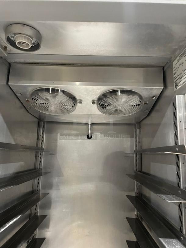 Commercial refrigerator interior with dual cooling fans, stainless steel shelves, and a control panel label on the upper right.