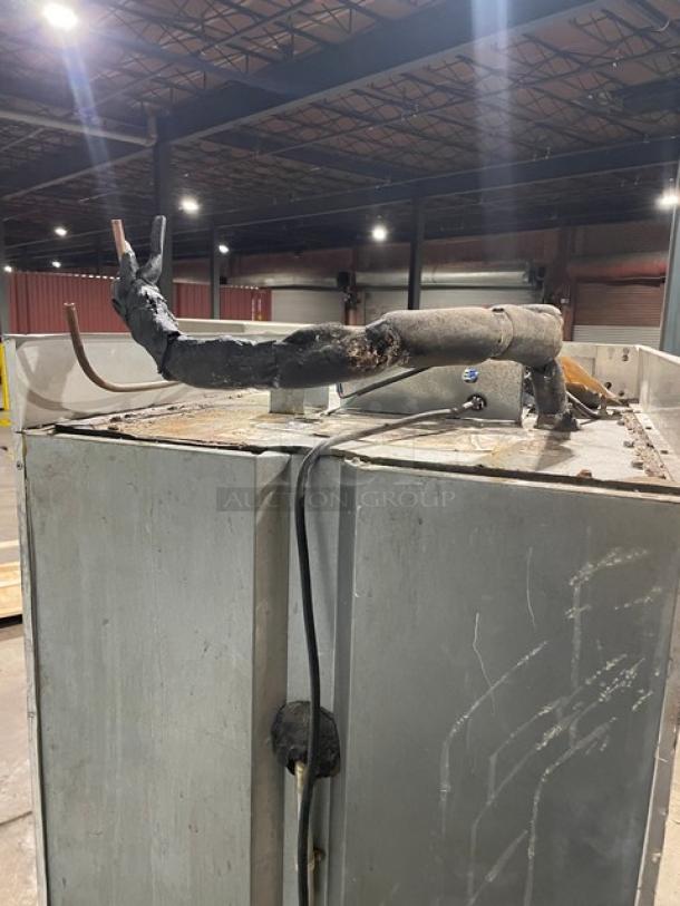 Large industrial metal unit with rusted pipes and wiring on top, in worn condition. Warehouse setting, no visible labels.