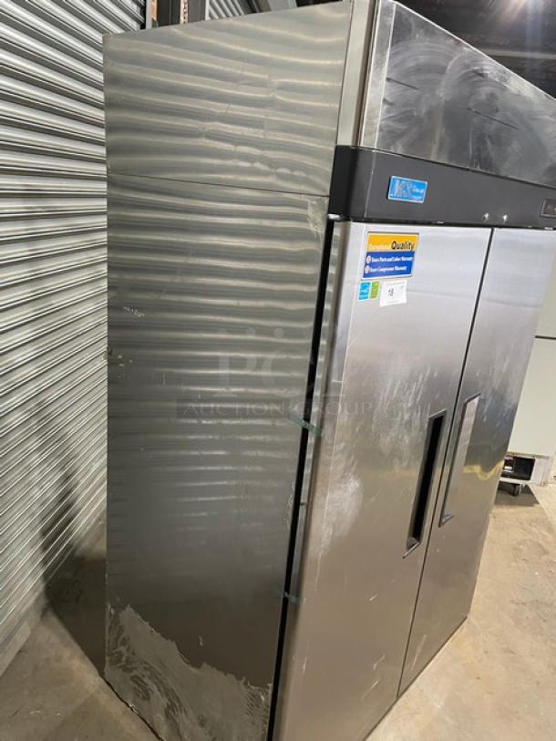 Commercial stainless steel refrigerator with double doors, visible wear, and quality inspection stickers.