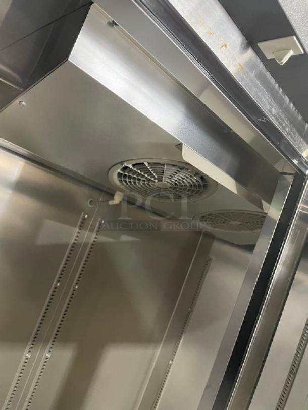 Stainless steel commercial refrigerator interior, features dual cooling fans, shelving racks. Clean and in good condition.