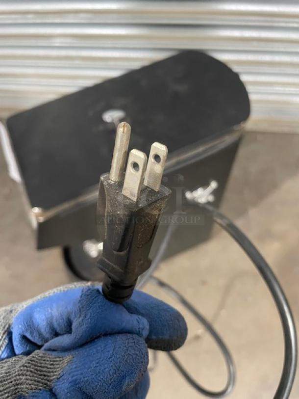 Power cord with three-prong plug connected to a black electrical device. Cord shows minor wear.