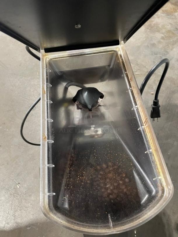Commercial coffee grinder with clear bean hopper, electric cord attached, showing moderate wear. No visible brand or model markings.