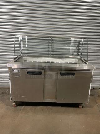 Stainless steel food prep counter with glass sneeze guard, two doors, caster wheels; brand "Lando", moderate wear visible.