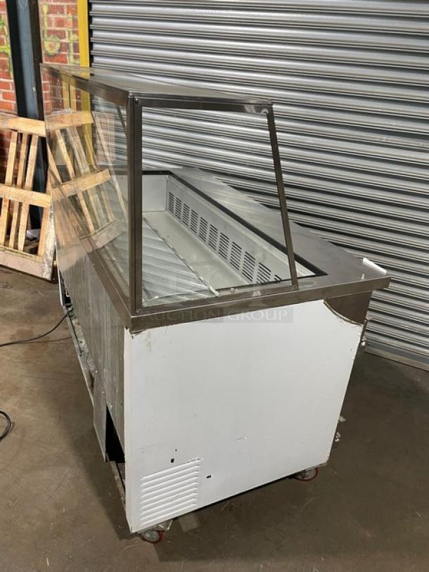 Commercial refrigerated display case, used condition, clear glass front, stainless steel frame, on casters, no visible brand.