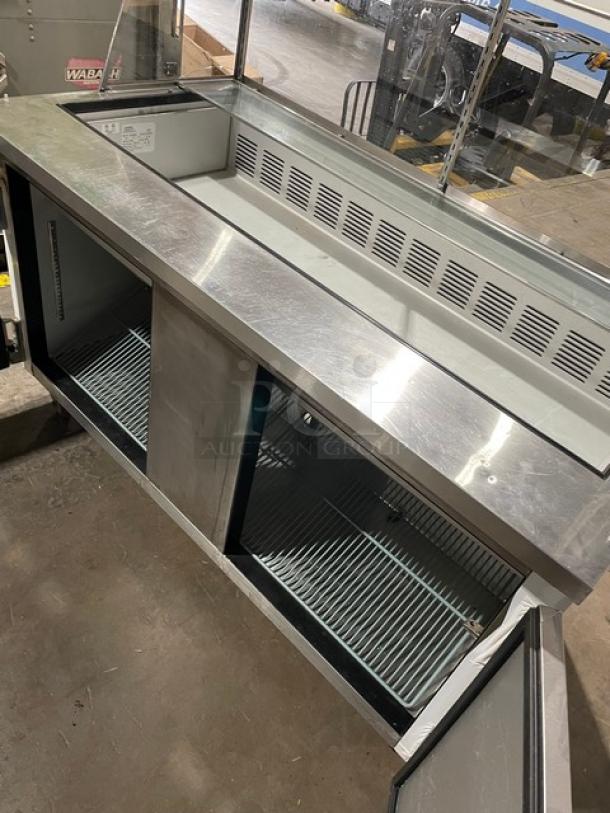 Commercial stainless steel refrigerated counter with glass top, dual-door, cooling vents, and internal shelving. Good condition.
