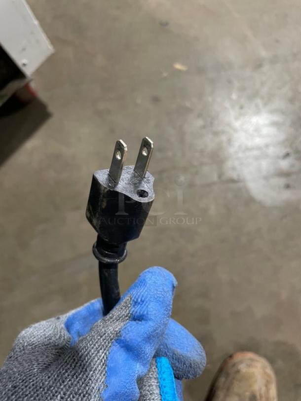 Two-prong electrical plug on a black cord held by a gloved hand. Appears in used condition.