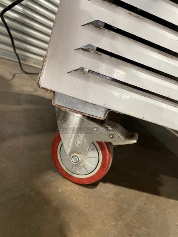 Industrial caster wheel with red rubber tire on metal base, attached to vented metal equipment. Appears used, sturdy.