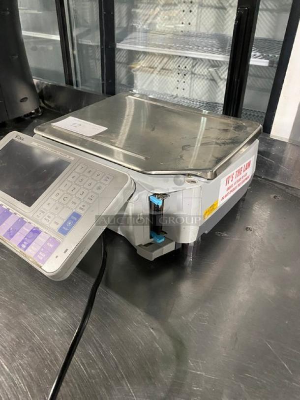 Digital retail scale with keypad, stainless steel platform, and power cable. Label reads: "It's the Law" for precise measurements.