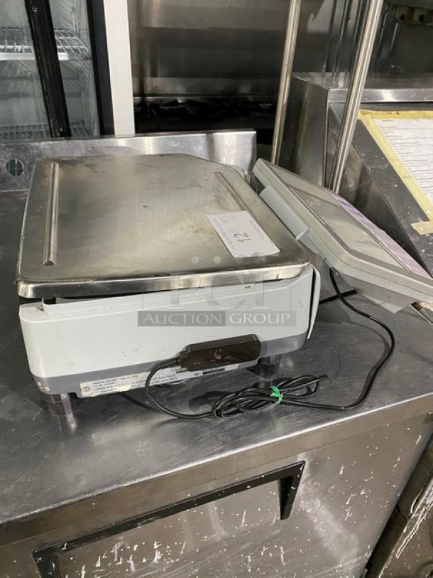 Commercial electric panini press, metal and white plastic, showing surface wear, with power cord. Tag reads "12".