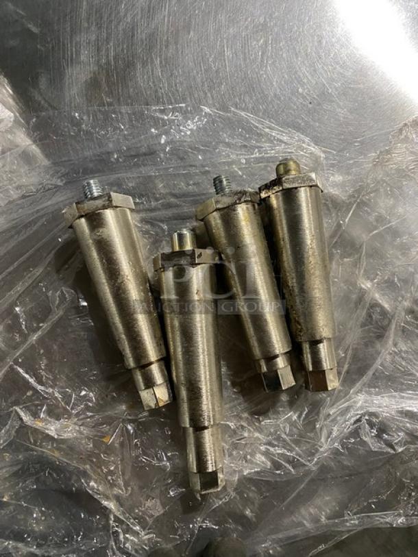 Four silver metal pin couplings on plastic wrap, showing slight wear, threaded ends visible, suitable for industrial use.