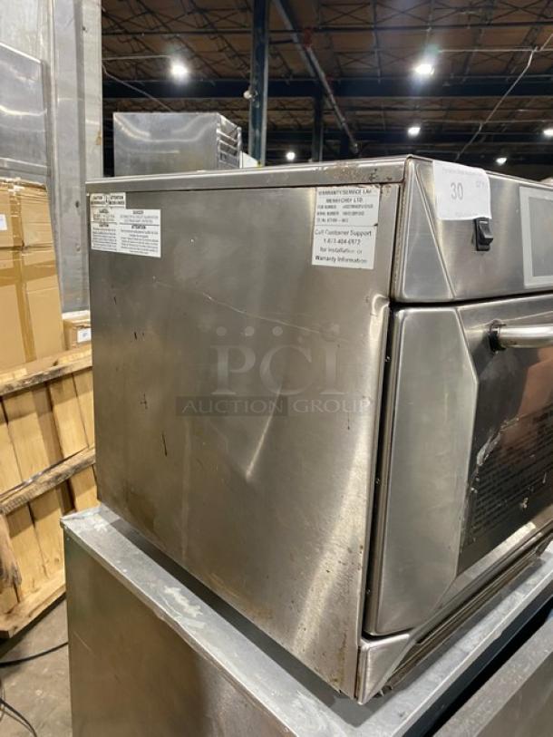 Commercial stainless steel oven with visible wear and scratches. Labels show model and warranty info. Auction lot number visible.