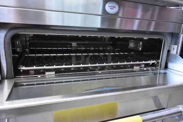 Stainless steel commercial oven with open door, interior shelves, and "Caution Hot" label. Excellent condition.