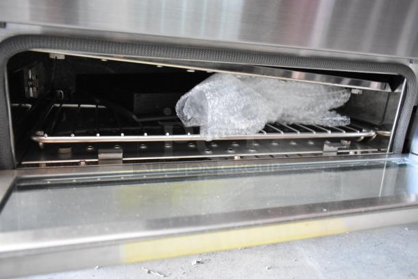 Stainless steel oven interior with a baking rack, partially covered in bubble wrap, indicating new or unused condition.