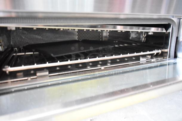 Stainless steel oven interior with baking tray and rack, in excellent condition. Features sleek design and clean surfaces.
