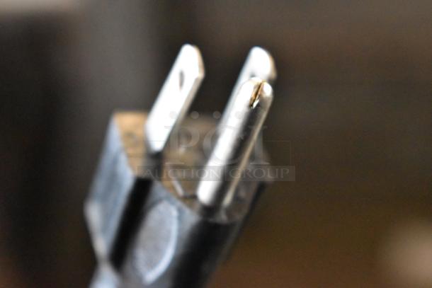 Close-up of a three-prong electrical plug with visible metal prongs. Condition appears used.