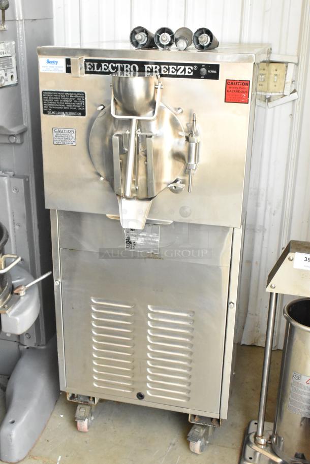 Electro Freeze ice cream machine, stainless steel, industrial model, visible caution labels, mounted on wheels, good condition.