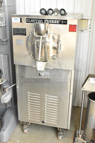 Electro Freeze ice cream machine, stainless steel, industrial model, visible caution labels, mounted on wheels, good condition.