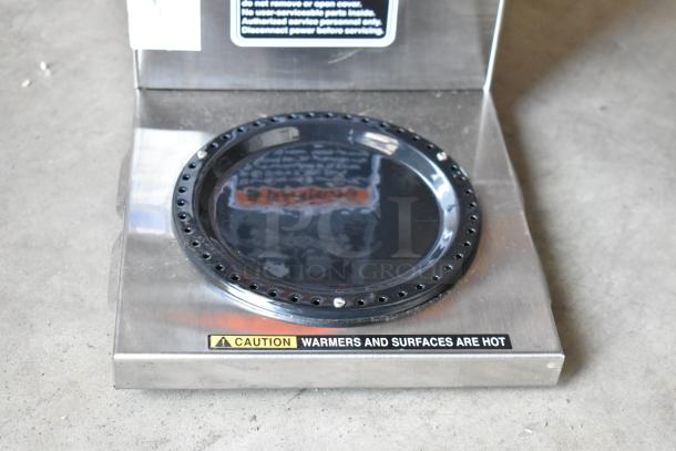 Stainless steel warming plate with a black circular surface. "Caution: Warmers and surfaces are hot" label on front.