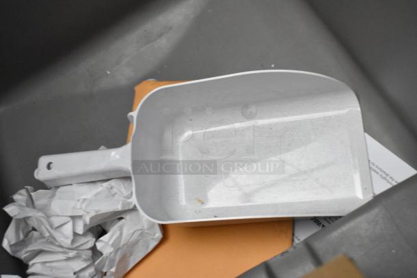 White plastic dustpan, slightly used, with some dirt and scratches, resting in a bin with crumpled paper nearby.