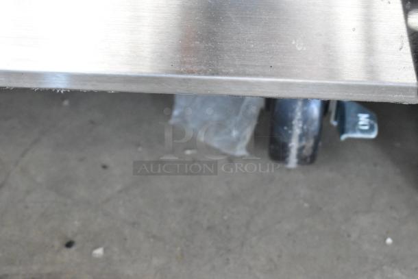 Close-up of stainless steel table edge on wheels, showing industrial design. Slight wear visible; suitable for heavy-duty use.