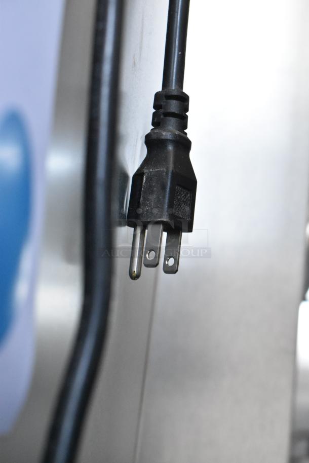 Close-up of a black electrical plug with three prongs attached to a cord, resting against a metallic surface.