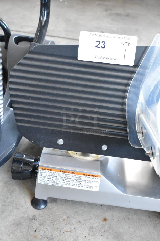 Commercial meat slicer with ribbed black cover and visible safety warnings. Tag labeled "23" from PCI Auctions.