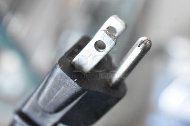 Close-up of a metal and plastic power plug with prongs, in good condition, highlighting the robust design and detail.