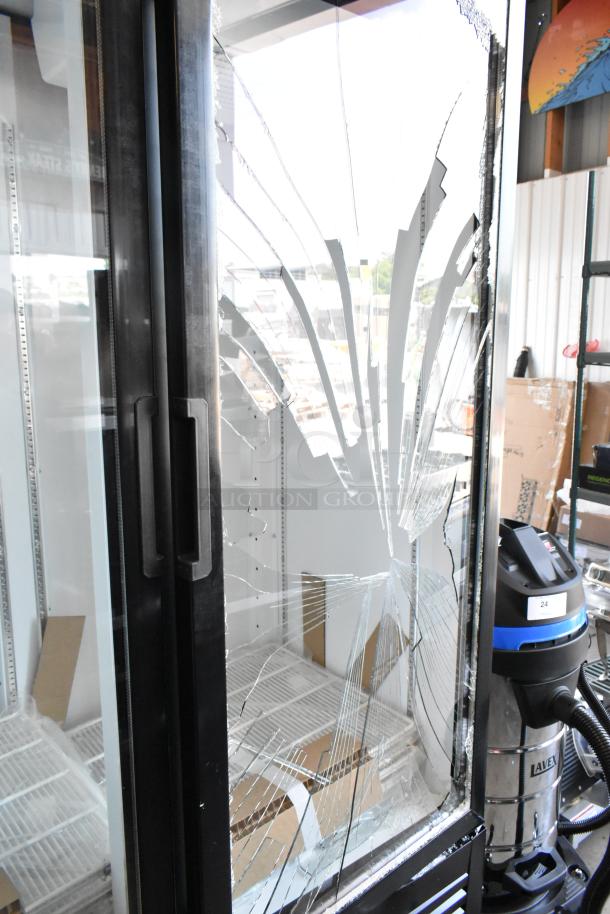 Commercial refrigerator with shattered glass door, metal frame, and two vertical handles. Interior shelves visible.