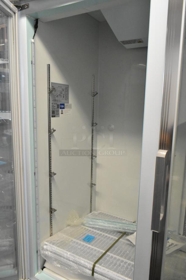 Commercial display refrigerator interior, includes adjustable metal shelving, new condition, instruction labels inside.