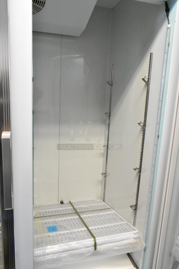 Commercial display refrigerator, unused condition, shelves wrapped in bubble wrap, adjustable metal racks, LED lighting.