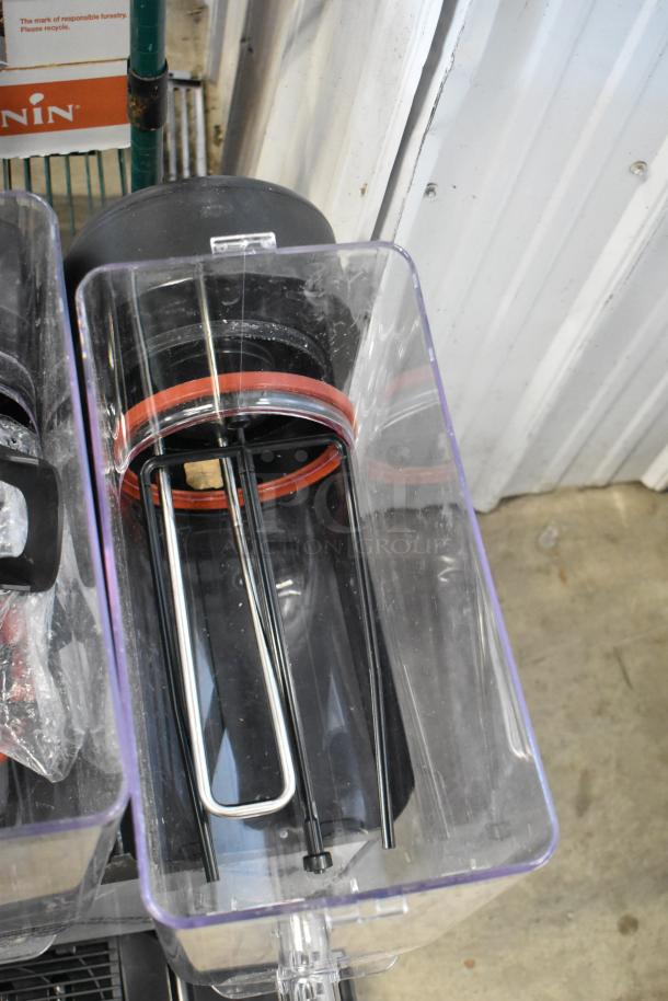 Clear plastic container with black and chrome metal components inside, featuring red rubber seals. Appears in used condition.